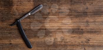 sharp open straight razor lying on a rough wooden background