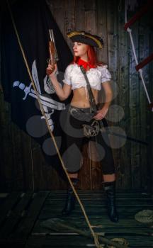 Young attractive armed girl pirate captain looks into the distance on the background of the flag Jolly Roger