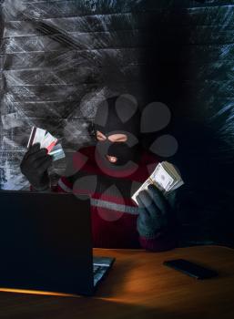 a bandit in a mask of a balaclava using a laptop does not fair profit on the Internet