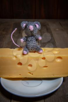 a small toy mouse the symbol of 2020 sits on a large piece of cheese with holes in a dark room