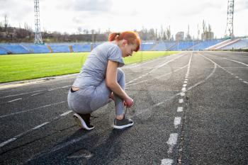 young girl getting ready for a run through the stadium and tying shoelaces on sports shoes
