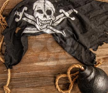 classic round black antique bomb with a long rope wick and a pirate flag Jolly Roger on a rough wooden background