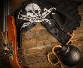 classic round black antique bomb with a long rope wick and a pirate flag Jolly Roger on a rough wooden background