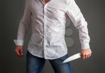 A man in a white shirt and jeans holds in his hands a large steel kitchen knife on a dark background