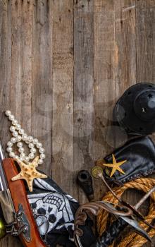 vintage pirate epee and pistol flag jolly roger and other medieval outfit lie on empty wooden background