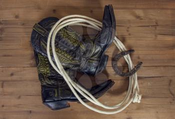 Shabby old ornate classic cowboy boots horseshoe and lasso on wooden background