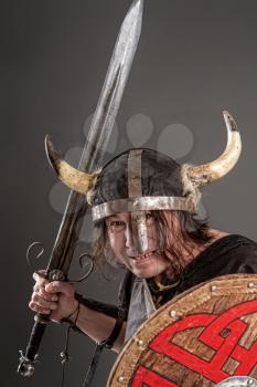 comical knight in a horned helmet with a shield and sword on a dark background