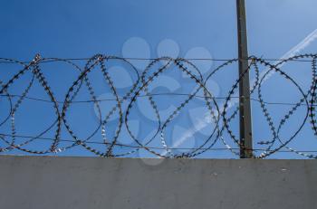 concrete wall and tangled iron barbed wire on blue sky background 