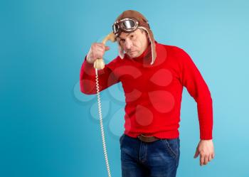 An adult man in a pilot's helmet and glasses communicates playfully and cheerfully on an old phone