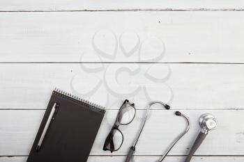 Workplace of doctor - stethoscope, notepad, glasses on wooden desk