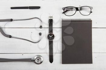 Workplace of doctor - stethoscope, notepad, glasses and watches on wooden desk