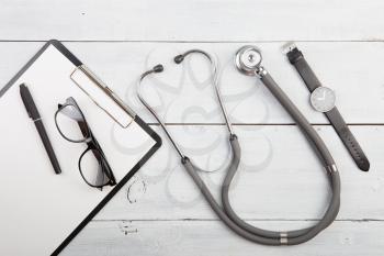 Workplace of doctor - stethoscope, medicine clipboard, glasses and watches on wooden desk