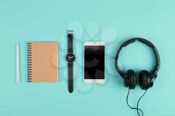 Smartphone, notepad, headphones, pen and watch on the blue background 