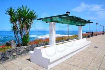 Ocean Promenade in Puerto de la Cruz, Tenerife, Spain with lamps and resting bench.