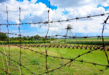 View through the barbed wire fence on watchtower and line of defense and military territory near state border. Memorial military area near Satov village in Czech Republic.