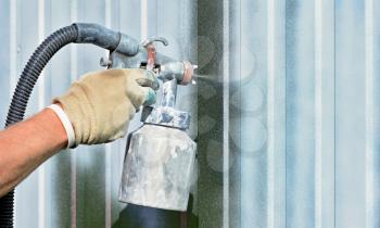 Spraying white paint onto a galvanized surface by an airbrush gun.