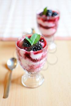 Glass cups with cream cheese blackberry desserts. Fresh blackberries and mint leaves are placed on top of the desserts.