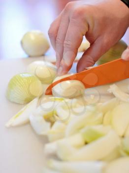 Hand holding orange ceramic knife and slicing the fresh onion into small pieces on cutting board.
