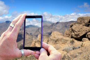 View over the mobile phone display during shooting Gran Canaria mountains. Holding the mobile phone in hands and taking a photo, focused on mobile phone screen.