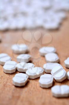 Macro of a White Pills on Wooden Brown Background.