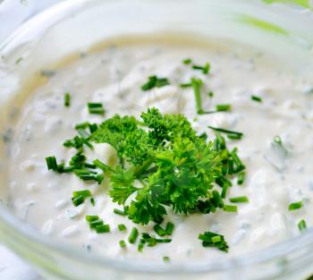 Glass bowl with garlic sour cream dressing sprinkled with fresh parsley.