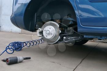 View of a disc brake during tyre replacement and pneumatic air screwdriver on the ground. Car maintenance.