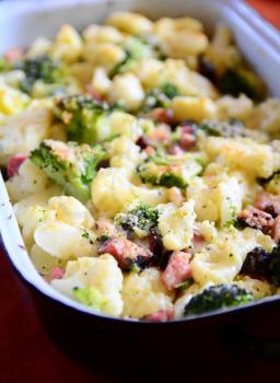 Baked Cauliflower and Broccoli with Grated Parmesan and Pieces of Bacon in Black Pan.