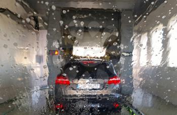 A view from car through wet glass of an another car in car wash.