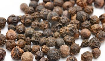 Closeup of whole black peppercorns on white background.