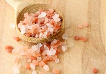 Scattered Pink Himalayan Rock Salt in Wooden Spoon on Wooden Background, top view.