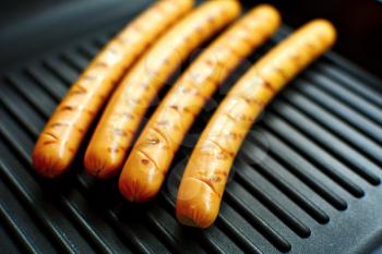 Closeup of a four sausages on a black grill pan.