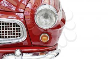 A front view of a red shiny vintage car, isolated on a white background. Part of a shiny red vintage car with headlight and grille, front view. 