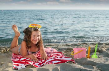 happy little girl with diving mask lying on beach