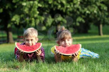 happy boy and little girl with watermelon lying on grass