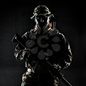 Bearded Special forces United States in Camouflage Uniforms studio shot half length. Holding weapons, wearing jungle hat, Shemagh scarf, he is ready to kill. Contour shot, backlit