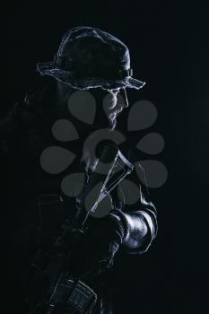 Half length studio contour backlight shot of bearded special forces soldier in uniforms with weapons, portrait on black background.