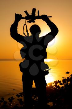 Army soldier with rifle above his head sunset silhouette. Victory concept