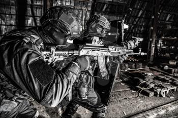 Police special forces, counter-terrorism tactical team fighters, private security company guards aiming guns while moving forward under cover of ballistic shield on anti narcotics raid, desaturated