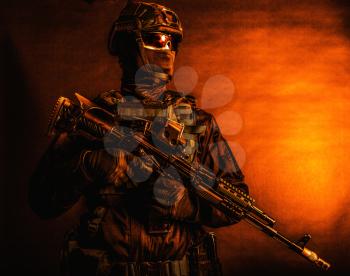 Half-length portrait of police tactical group fighter, special forces soldier, security service guard in mask and full ammunition, standing with assault rifle, low key studio shoot with red backlight