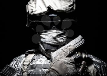 Special operations forces soldier in combat helmet with hidden behind balaclava and dark glasses face posing with sidearm service pistol in hand. Brown tone, high contrast, cropped on black background