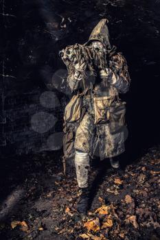 Post apocalyptic survivor, mysterious underground creature, stalker in gas mask and rags with runes, armed with handmade gun, hiding in dungeon, abandoned tunnel or city dark catacombs, sepia toned