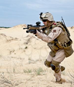 US soldier runs through the desert shooting a gun with grenade launcher