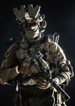 Anti-terrorist squad fighter, army elite forces soldier in combat uniform and tactical ammunition, armed mini submachine gun, wearing night-vision device, low key studio portrait on black background