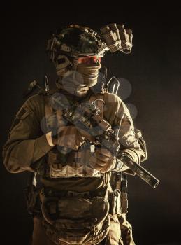 Anti-terrorist squad fighter, army elite forces soldier in combat uniform and tactical ammunition, armed mini submachine gun, wearing night-vision device, low key studio portrait on black background