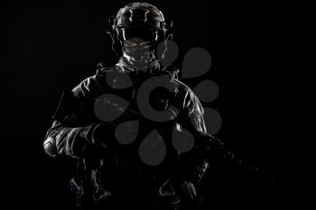 Army special operations forces soldier in mask and combat uniform, armed submachine gun, low key studio portrait on black, copyspace contour shot