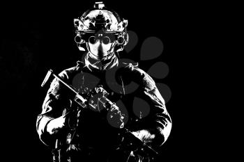 Army elite soldier with hidden behind mask and glasses face, in full tactical ammunition, equipped night vision device, radio headset, armed short barrel service rifle studio contour shot