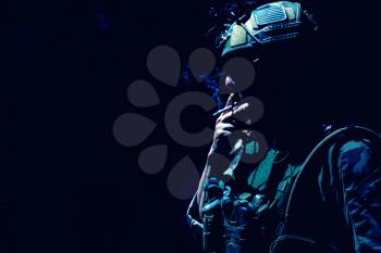 Army soldier in combat uniform and helmet, smoking cigarette in darkness. Special operations forces fighter, resting infantryman silhouette with cigarette in mouth and tobacco smoke, low key