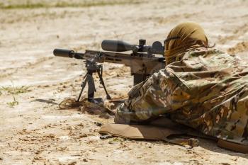 Young male sniper in camouflage with gun in the desert