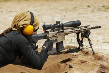 Young female sniper in camouflage with gun in the desert