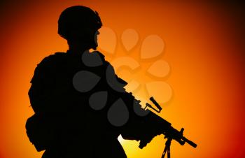 Silhouette of army infantry soldier, commando in combat helmet, armed light machine gun, standing on background of ocean horizon and sunset. Marine Corps rifleman, special forces shooter on sea shore